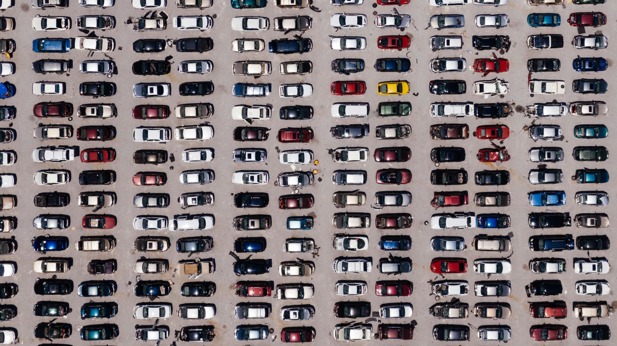 Aerial view of a large parking lot filled with rows of parked cars in various colors and models, aligned in organized rows.